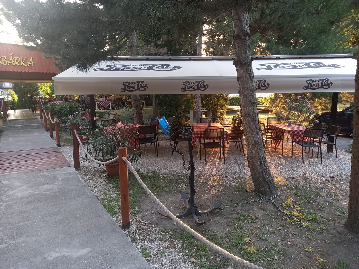 A Bárka étterem kerthelyisége piros kockás abroszos asztalokkal, fenyők között