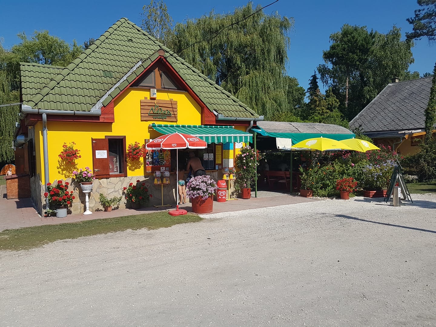A Nádas vendéglő sárga épülete napernyőkkel és virágokkal