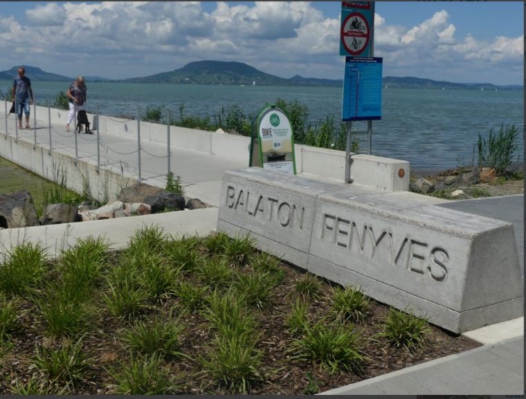 A balatonfenyvesi parti sétány a település nevét viselő kőtömbbel, háttérben a vízzel